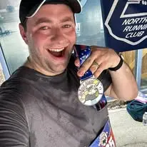 Joseph smiling with a race medal beside a Northeast Running Club banner